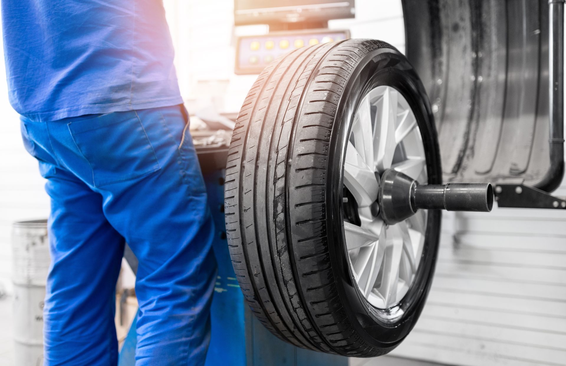 A technician wearing a blue uniform uses a professional balancing machine to service a car tire in an auto repair shop.