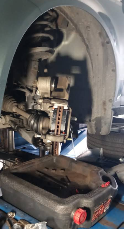 A car with the wheel removed, exposing the brake rotor and caliper suspended over a black oil drain pan.