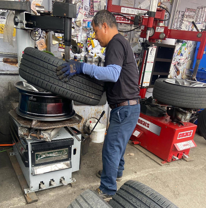 A person using a tire changer machine to mount a tire onto a vehicle wheel in an automotive shop.