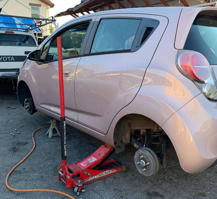A light pink car jacked up on blocks, with its front and rear wheels removed, parked on an outdoor paved surface.