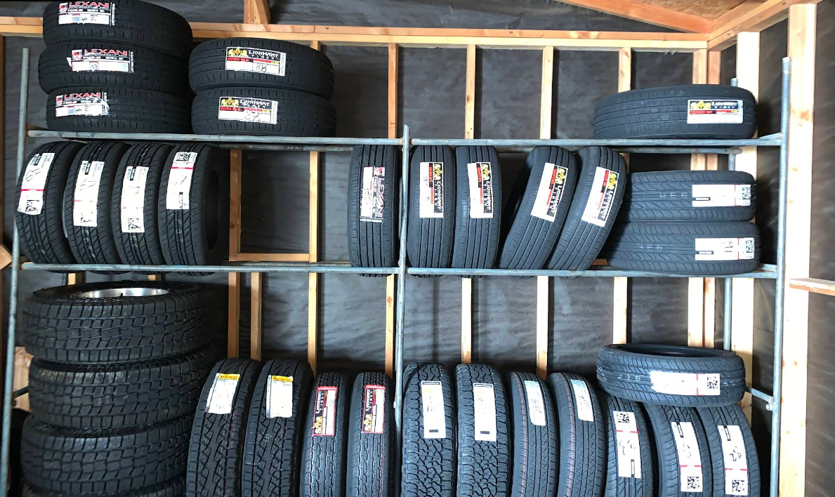 Shelves stacked with various black rubber tires arranged in a storage room with wooden wall studs.
