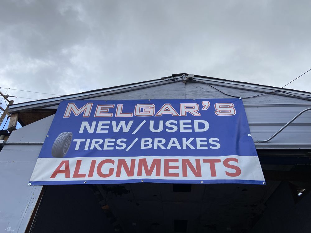 A blue and white banner for Melgar's advertising new/used tires, brakes, and alignments hanging above a shop entrance.