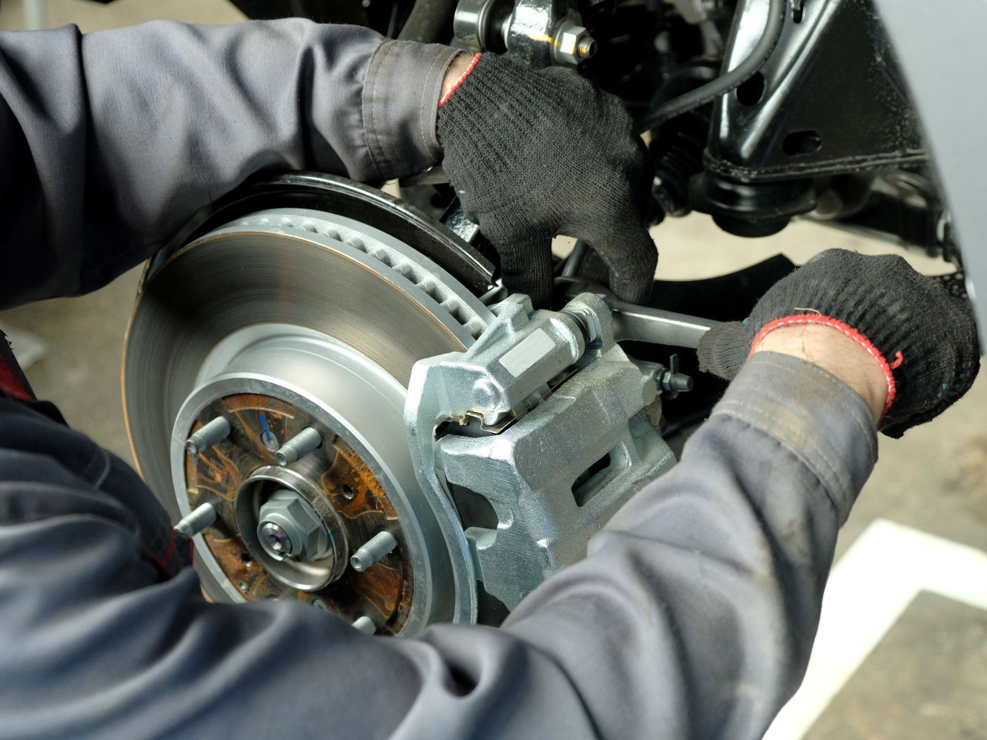 A mechanic wearing work gloves uses a wrench to tighten or adjust the brake caliper on a vehicle's disc brake assembly.
