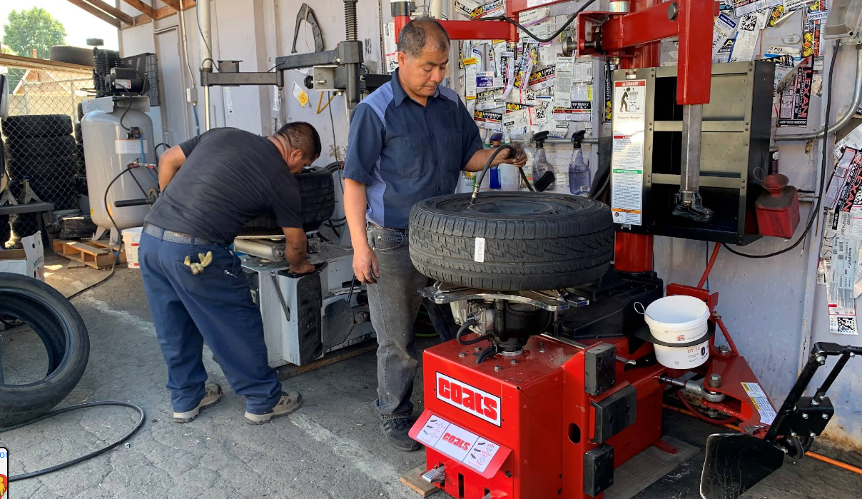 Two people work with a tire changing machine inside an auto repair shop.