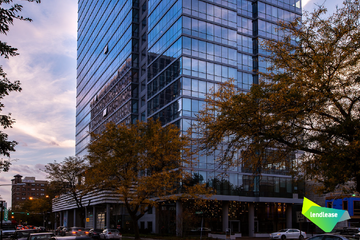 A tall building with a lot of windows is surrounded by trees and cars.