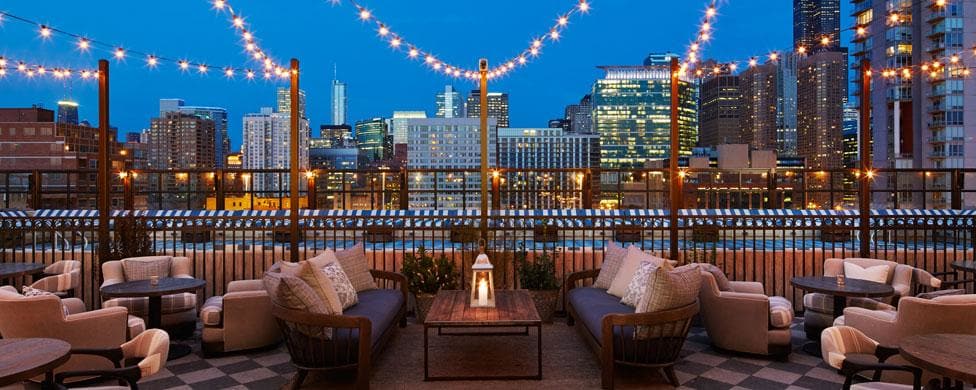 A rooftop bar with a view of the city skyline at night.