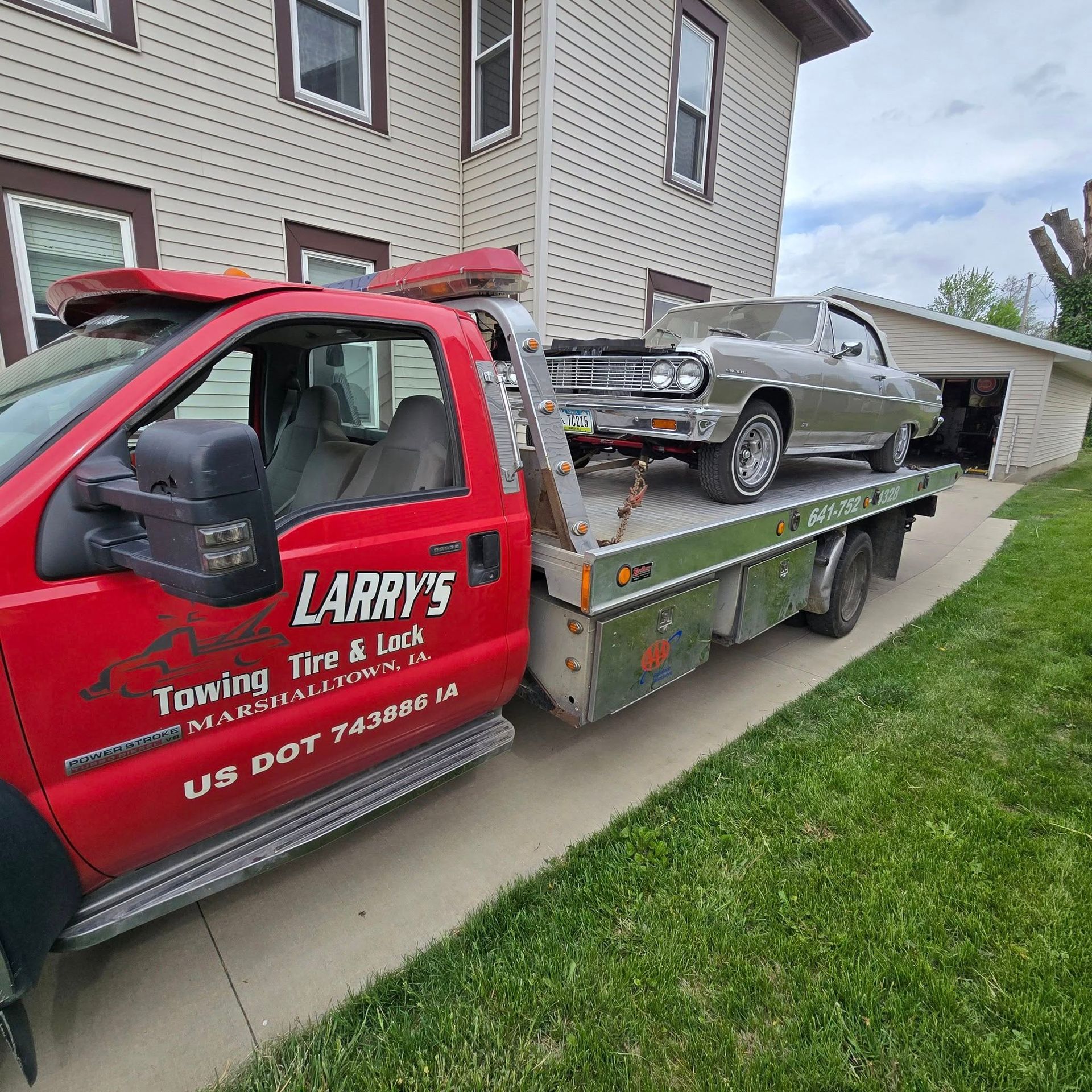 A red towing truck with a car on the back is parked in front of a house.