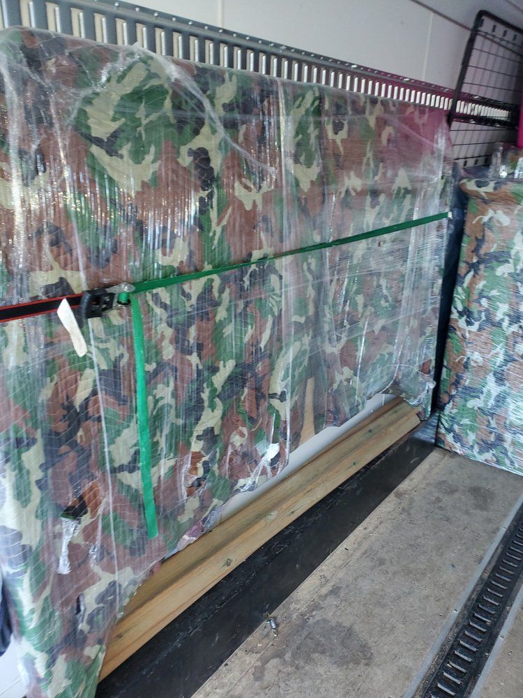 Camo-covered mattresses secured with plastic wrap and straps inside a cargo trailer.