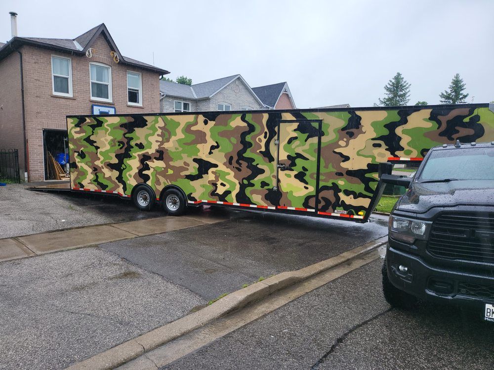 Large camouflage trailer parked on a wet driveway.