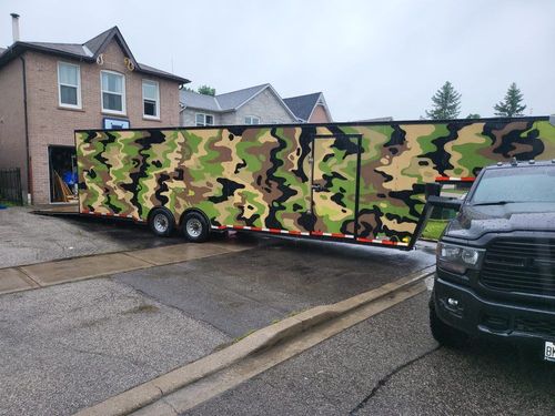 Large camo-wrapped trailer parked on a wet street.