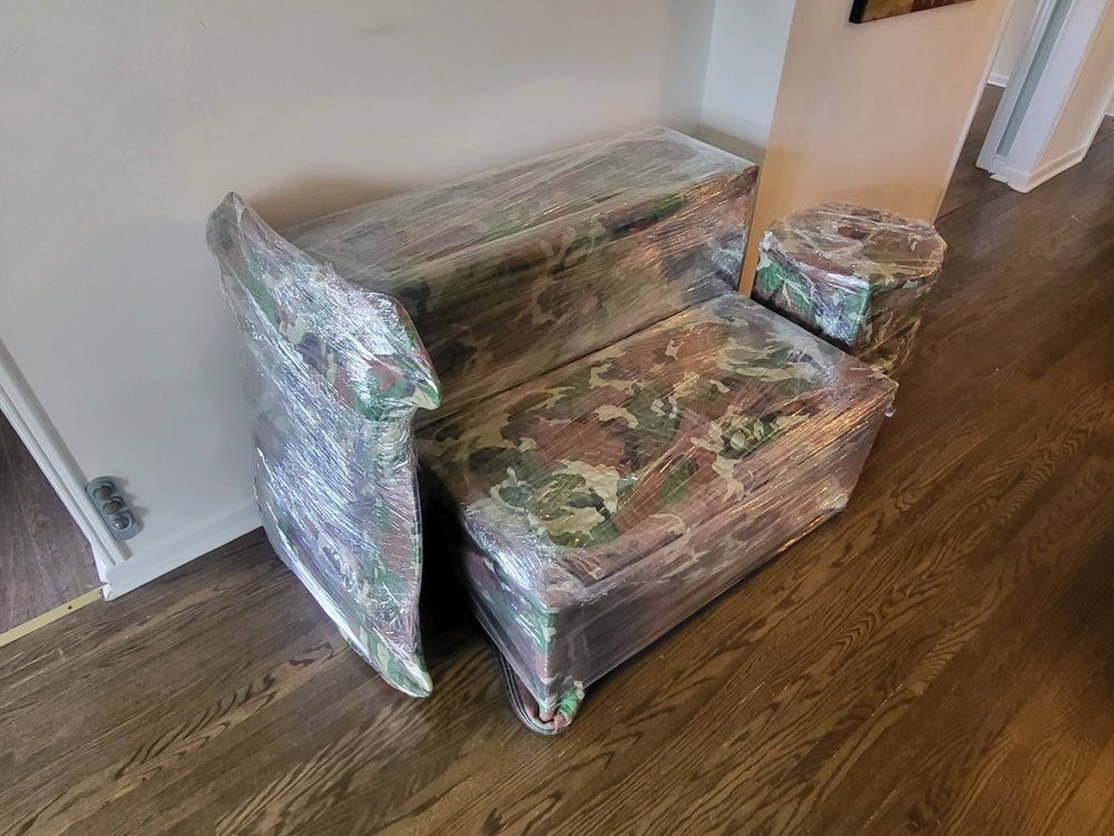 Camo-patterned furniture wrapped in plastic, ready for transport, on a hardwood floor.