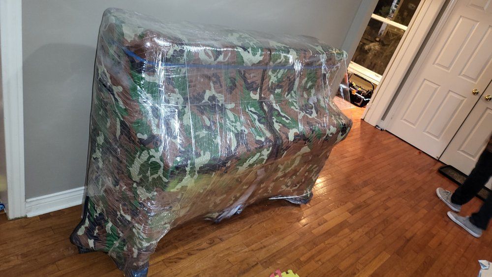 Wrapped piano, camouflage fabric, on hardwood floor, in a room with white door.