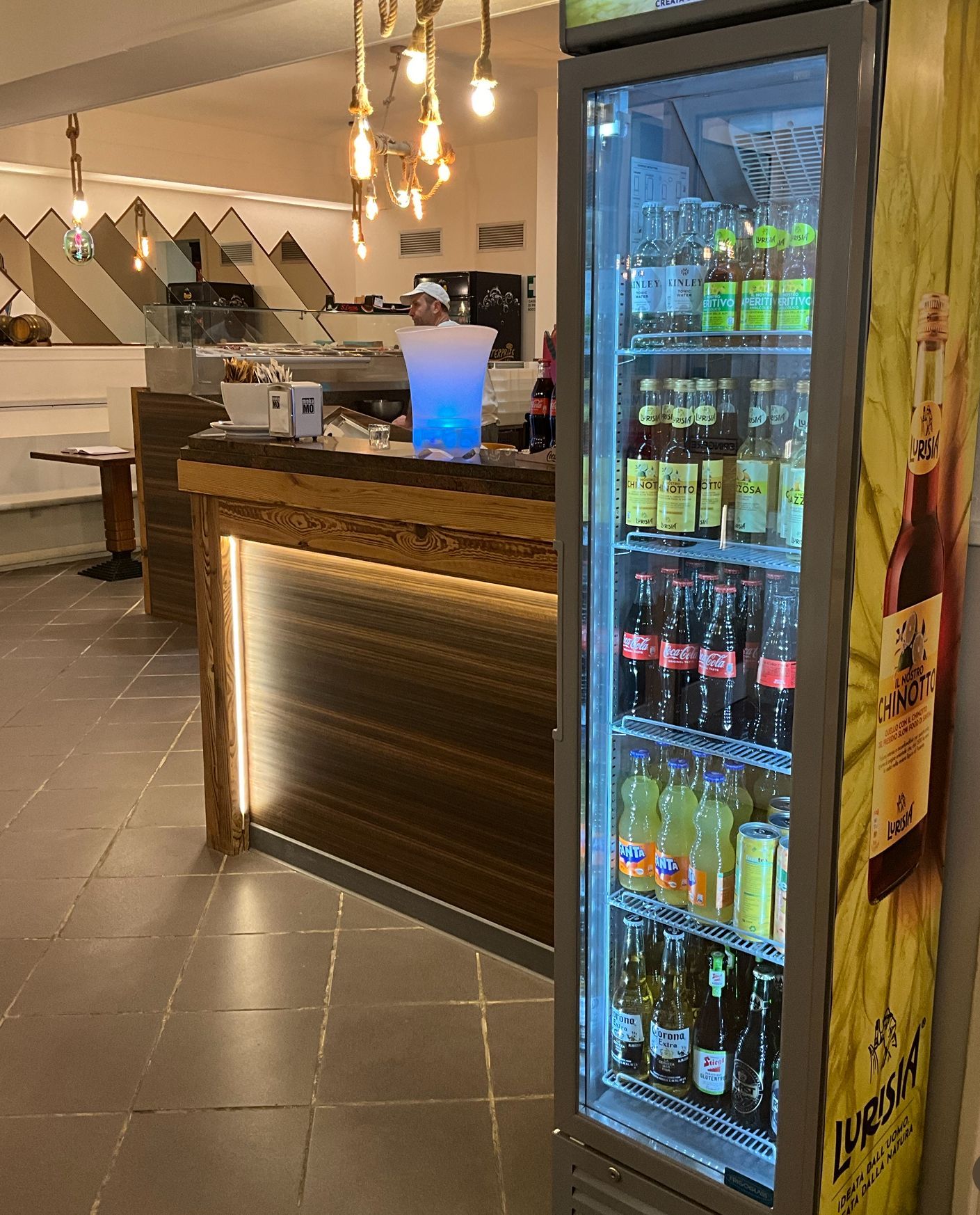 Un frigorifero pieno di bottiglie di soda è accanto al bancone di un ristorante