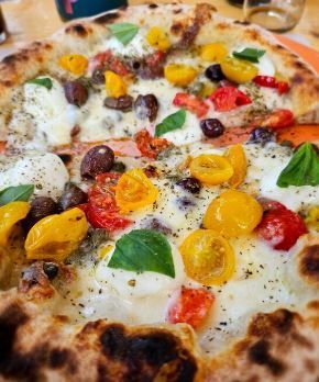 Una pizza con pomodori, olive, formaggio e basilico