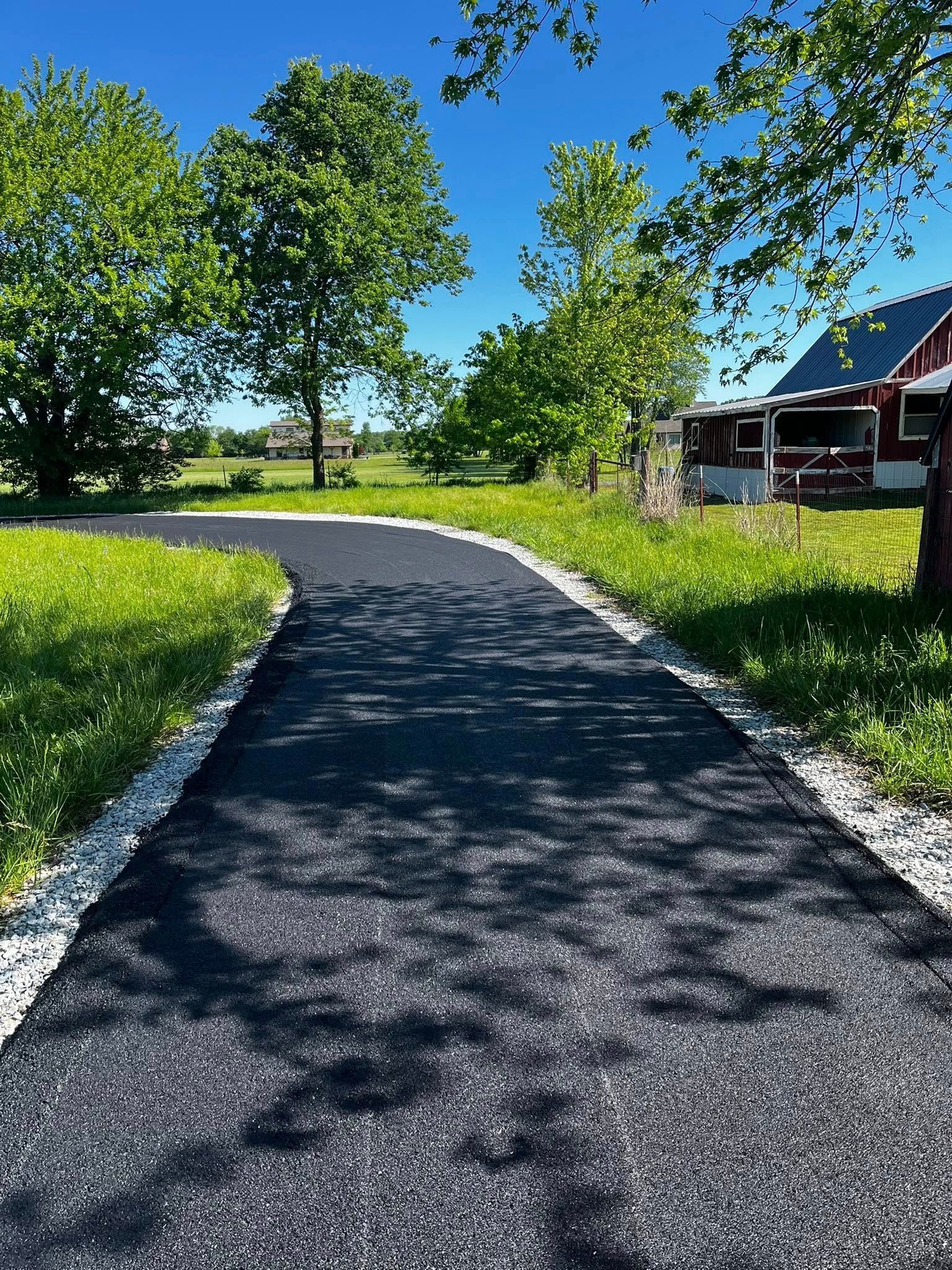 A road going through a grassy field with a red barn in the background.