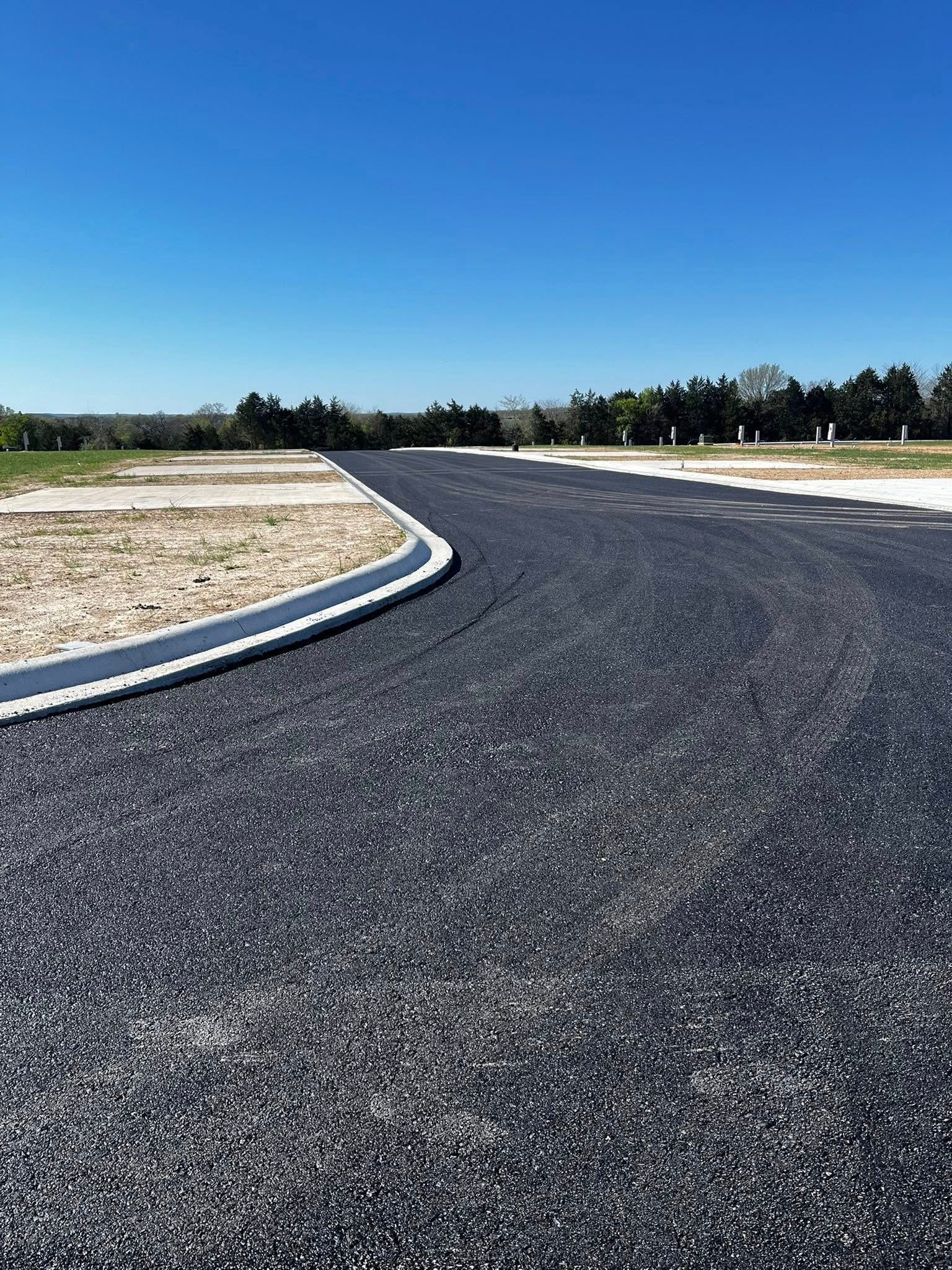 A black asphalt road with a white curb and trees in the background.