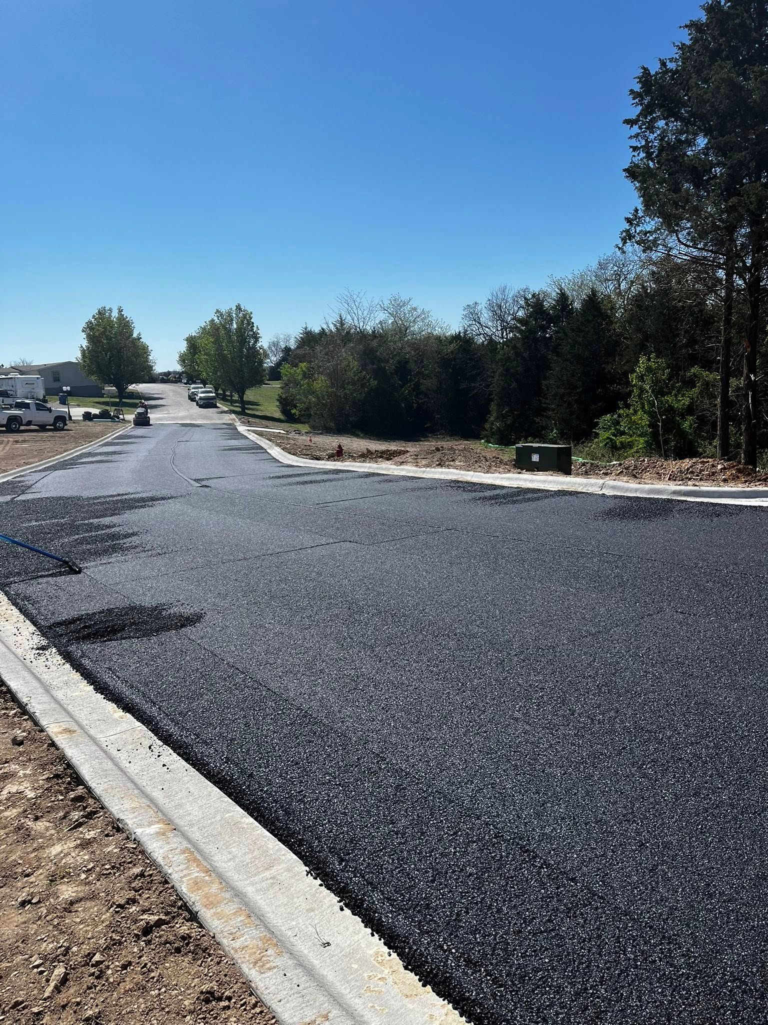 A black asphalt road with trees on the side of it and a blue sky in the background.