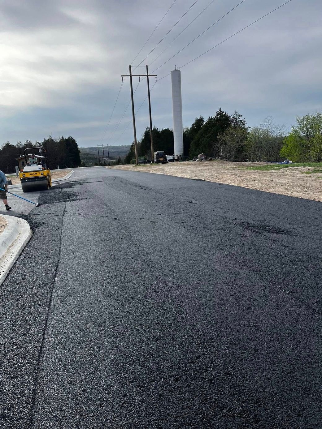 A road is being paved with a roller and a tower in the background.