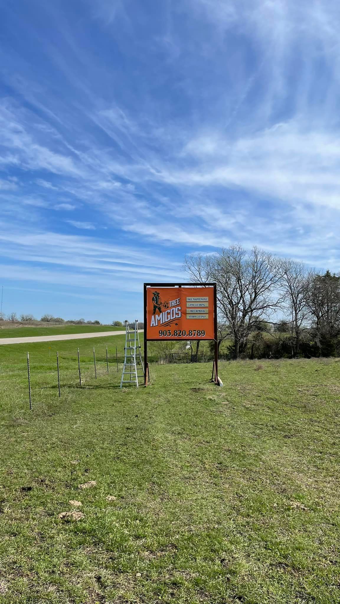 Sign with orange and black text on a green field under a blue sky.