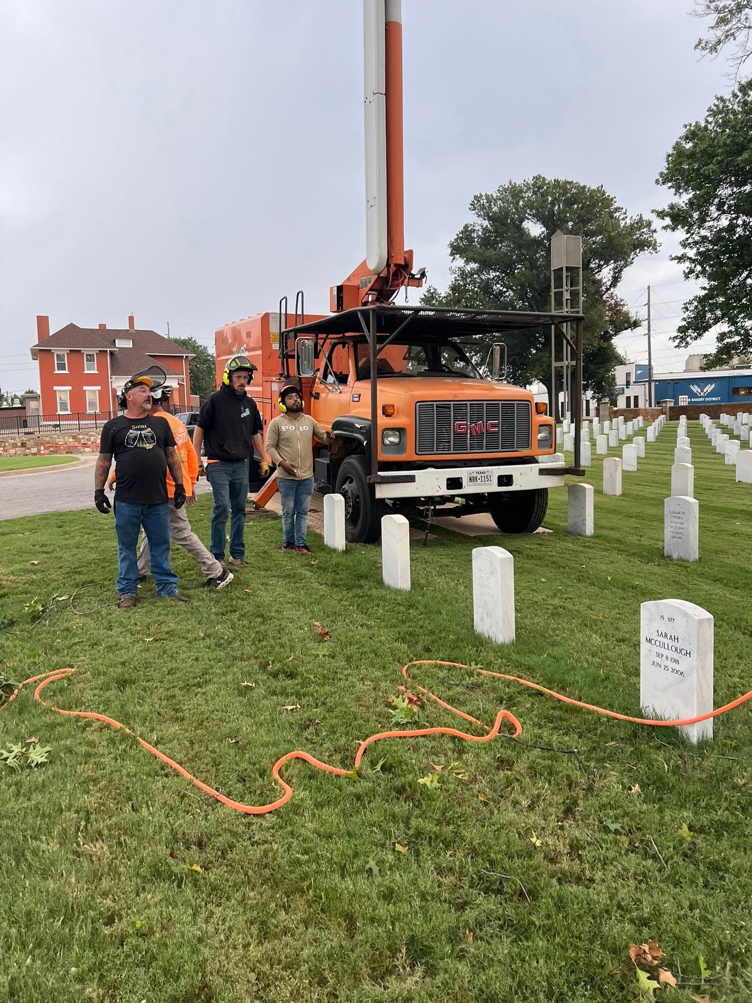 Men standing near orange truck with raised boom in a cemetery.