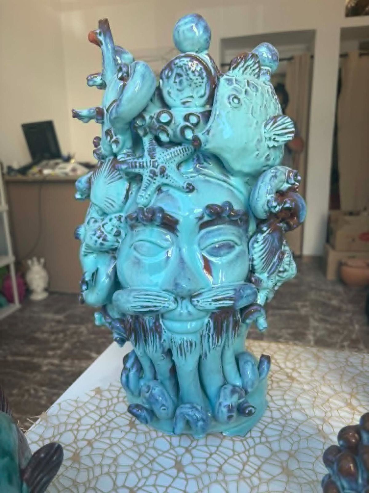 Sculture in ceramica blu e marrone esposte in una vetrina, tra cui un volto e forme simili ad alberi.