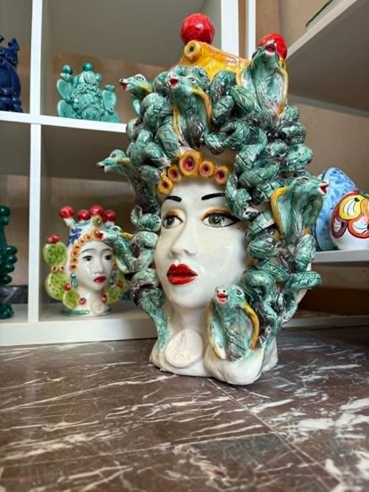 Tre teste di ceramica scura con decorazioni di frutta sono poste davanti a un muro di pietra; al centro c'è un oggetto a forma di ananas.