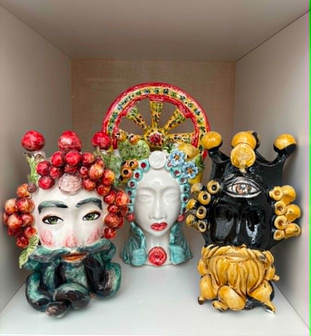 Coppia di vasi in ceramica ornati, raffiguranti una testa maschile e una femminile, con dettagli colorati, di fronte a un muro di pietra.