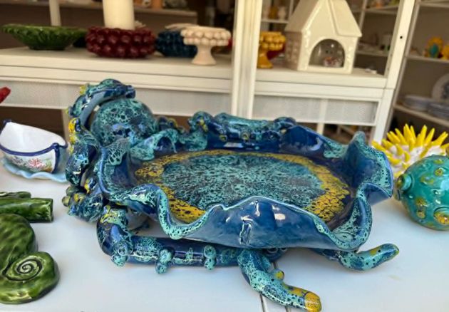Scultura in ceramica blu raffigurante un pesce su una mensola bianca.