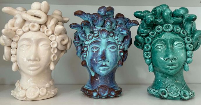 Vasi in ceramica a forma di testa con volti dettagliati, gioielli e decorazioni di frutta, su un tavolo di legno.