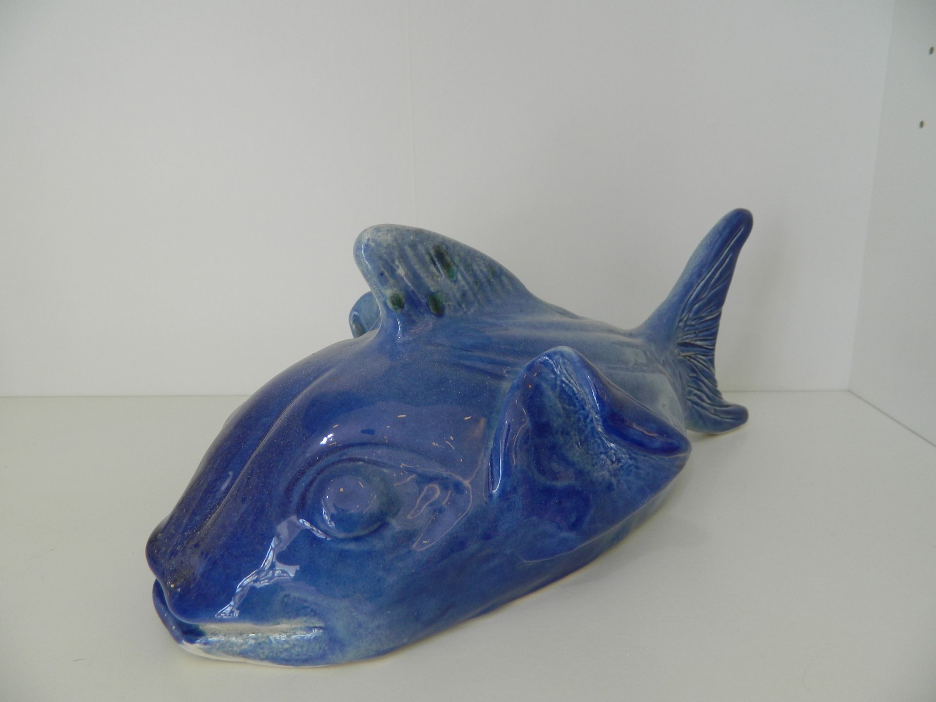 Scultura in ceramica blu raffigurante un pesce su una mensola bianca.