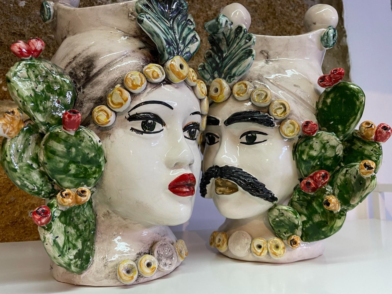 Teste di vasi in ceramica raffiguranti una donna e un uomo, ciascuna con dettagli floreali e di cactus.