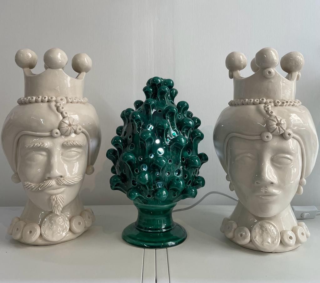 Sculture in ceramica raffiguranti teste di re e di regina con una pigna in ceramica verde tra di esse.