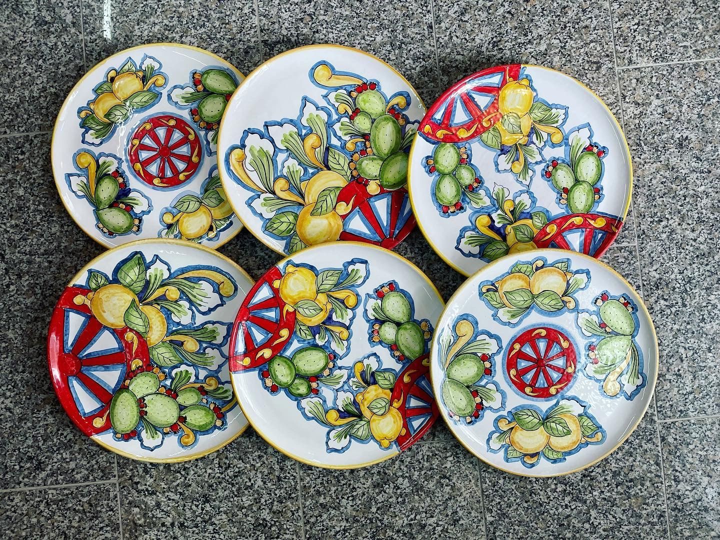 Sei piatti bianchi con motivi floreali e di cactus. Dettagli rossi, gialli e blu su una superficie grigia.