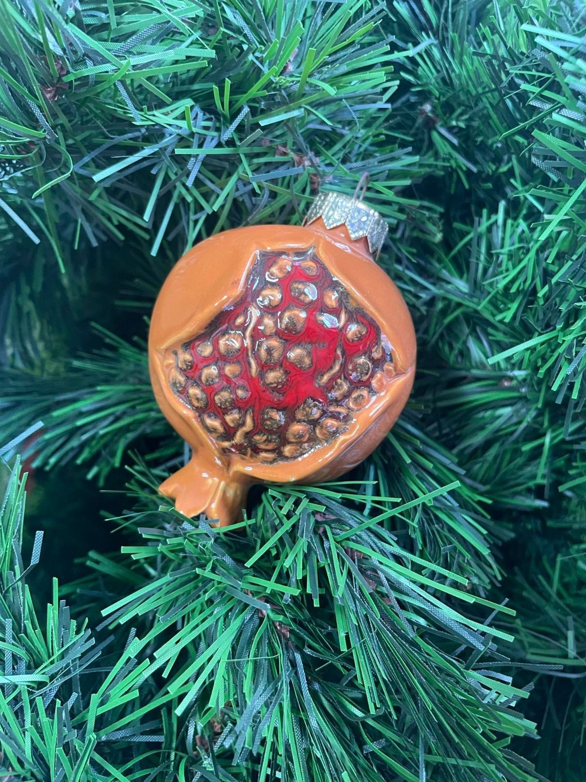 Decorazione raffigurante un melograno arancione con semi rossi, appeso a un albero di Natale verde.
