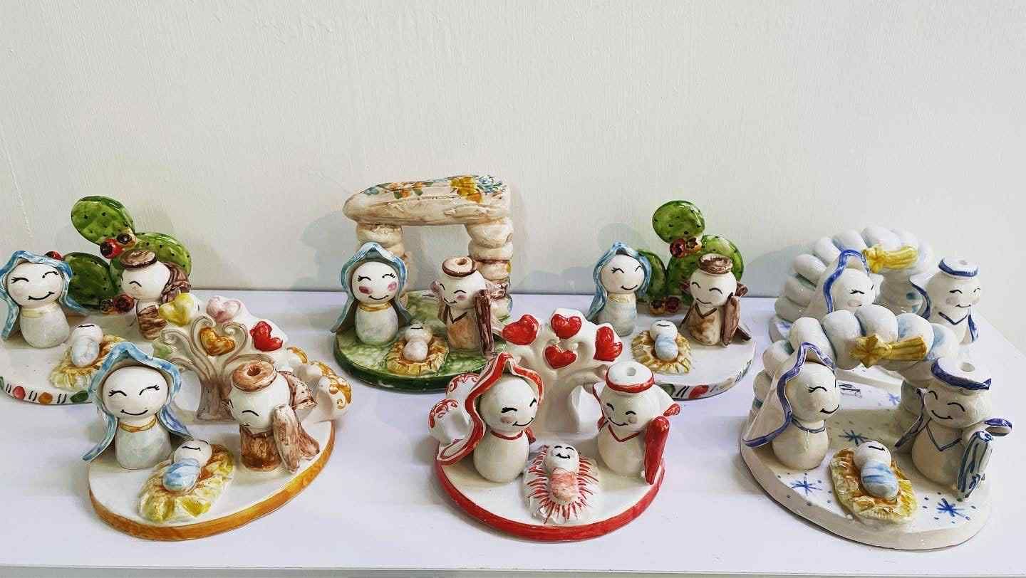 Presepi in ceramica con figure dipinte, in vari colori, esposte su una superficie bianca.