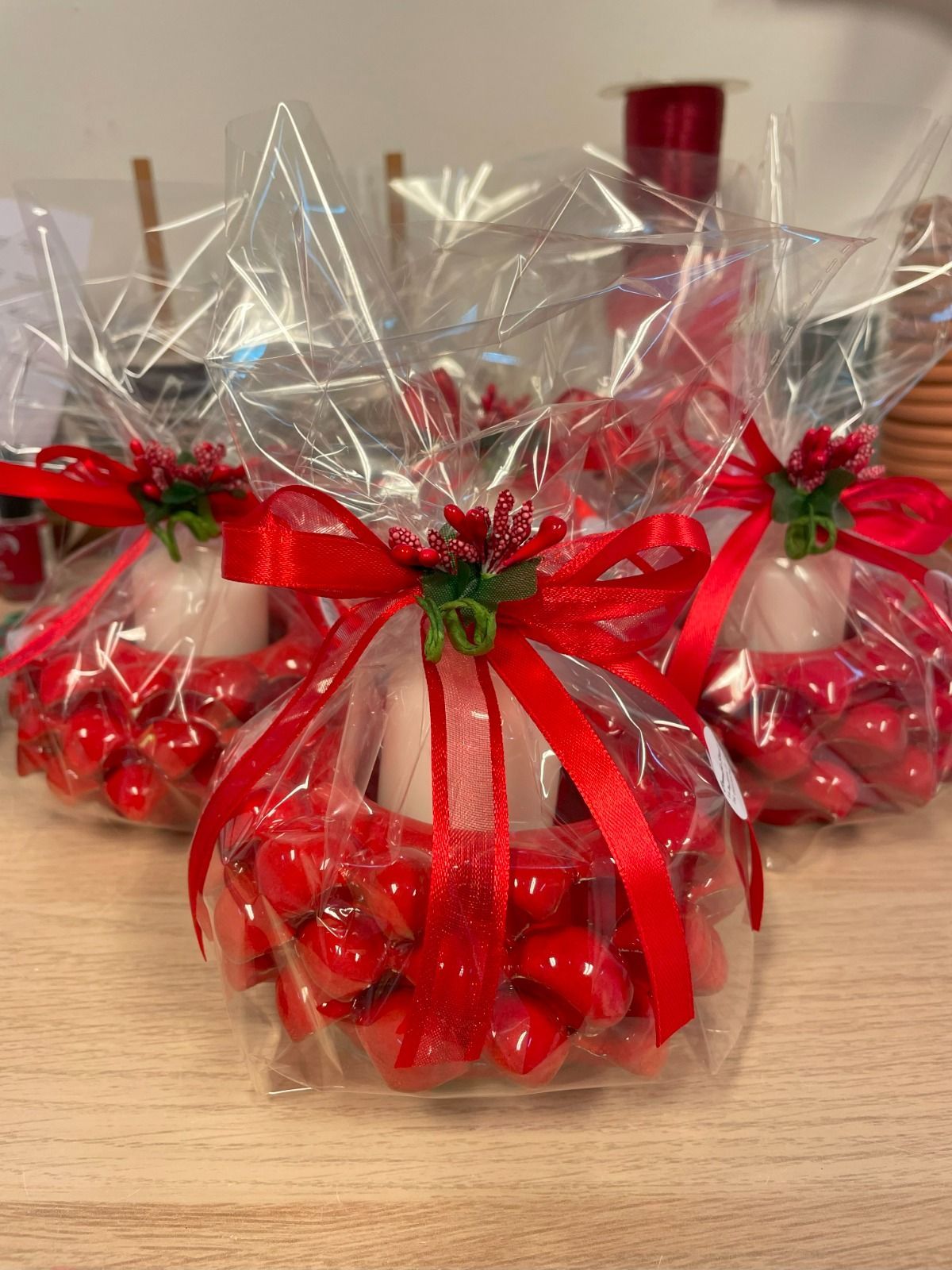 Tre regali incartati, ciascuno con una corona rossa a forma di cuore attorno a una candela, legata con un nastro rosso e del verde.