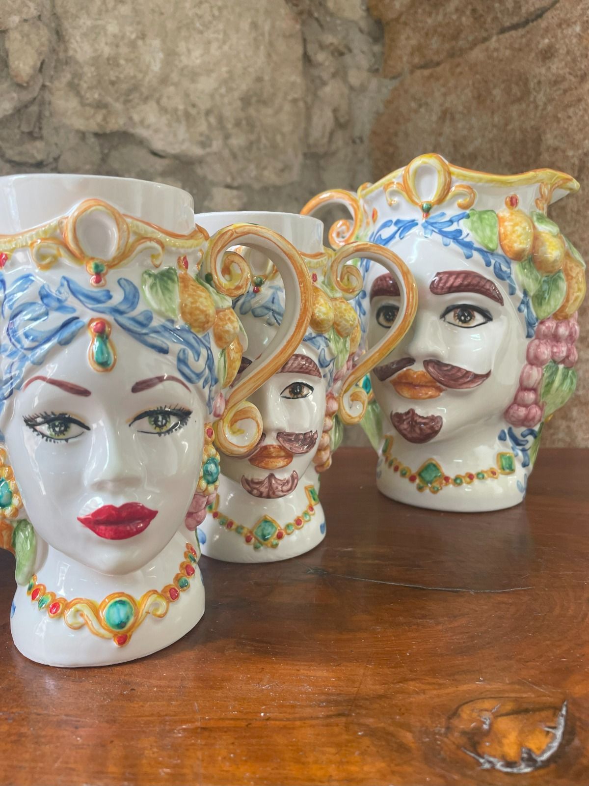 Brocche in ceramica a forma di testa con dettagli decorati e accenti colorati, su una superficie in legno.