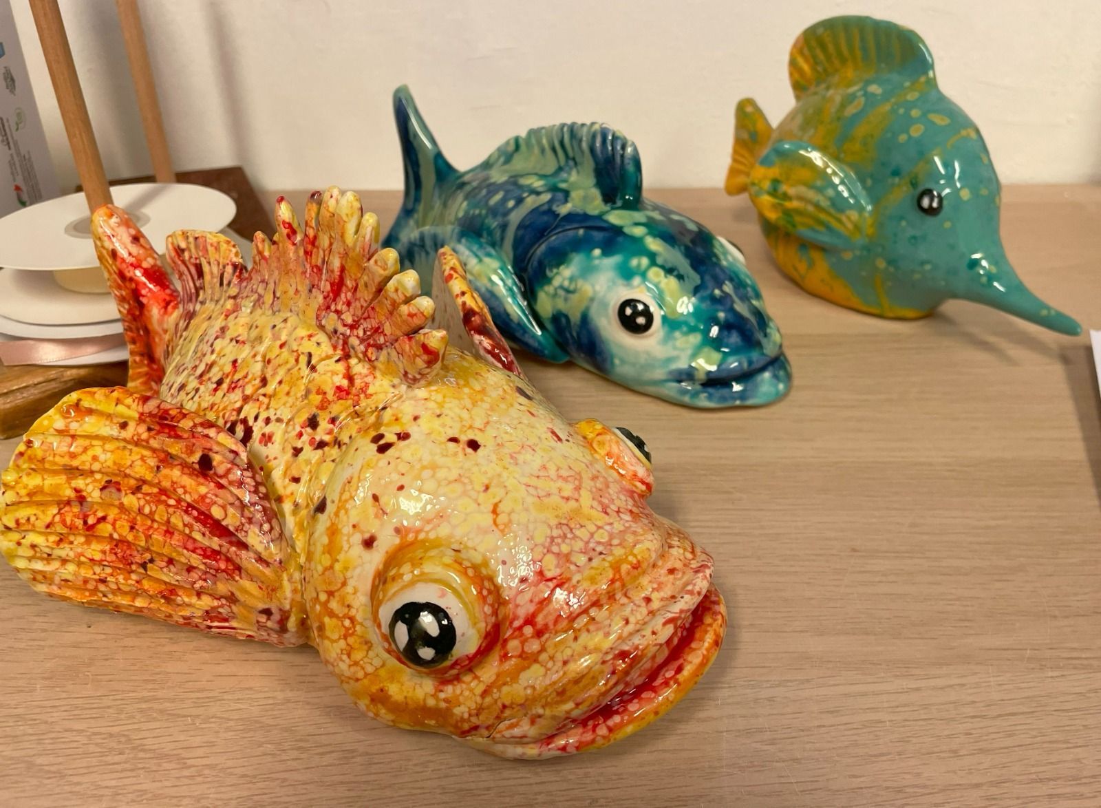 Tre sculture di pesci in ceramica colorata su una superficie di legno.
