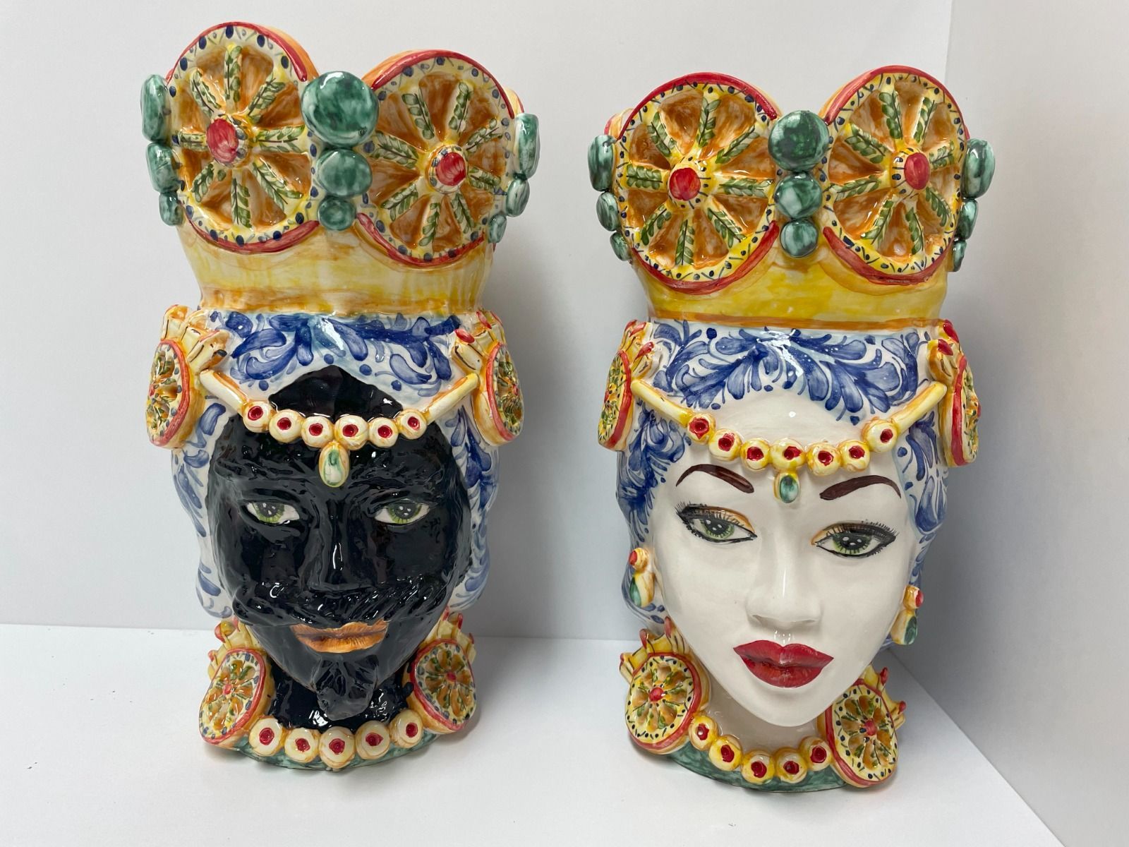 Due vasi in ceramica a forma di testa con corone ornate. Uno con la superficie nera, l'altro con la superficie bianca. Entrambi decorati con gioielli e colori vivaci.