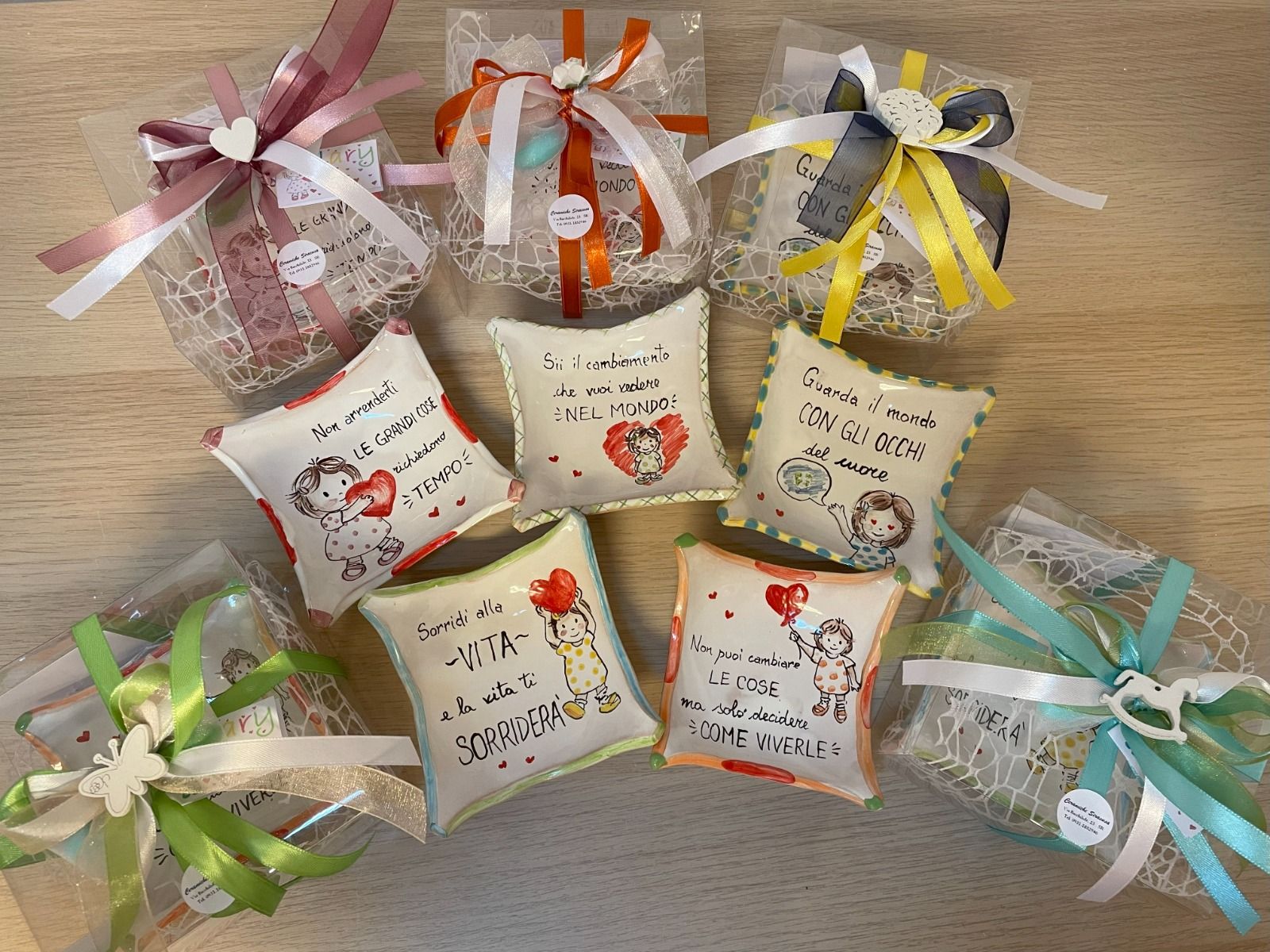 Piccole buste regalo decorate e bomboniere a forma di cuscino con illustrazioni e messaggi di angeli, legate con nastri colorati.