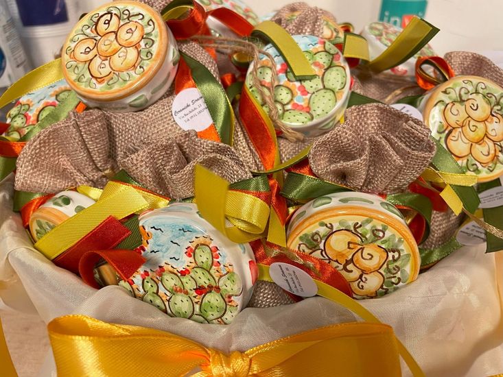 Disposizione di contenitori decorativi in ceramica con motivi di cactus e arance in un cestino, legati con nastri colorati.