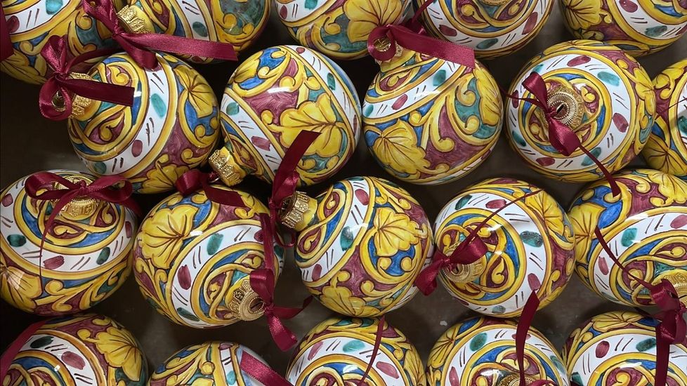 Palline ornamentali in ceramica con motivi floreali gialli, rossi e blu e fiocchi di nastro rosso.