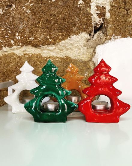 Quattro portacandele a forma di albero di Natale nei colori bianco, verde, arancione e rosso, ognuno con una candela accesa.