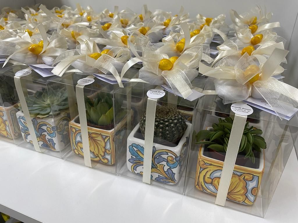 Cinque sacchetti portaconfetti fatti a mano color crema, un rosario e un ornamento floreale su una superficie di legno.