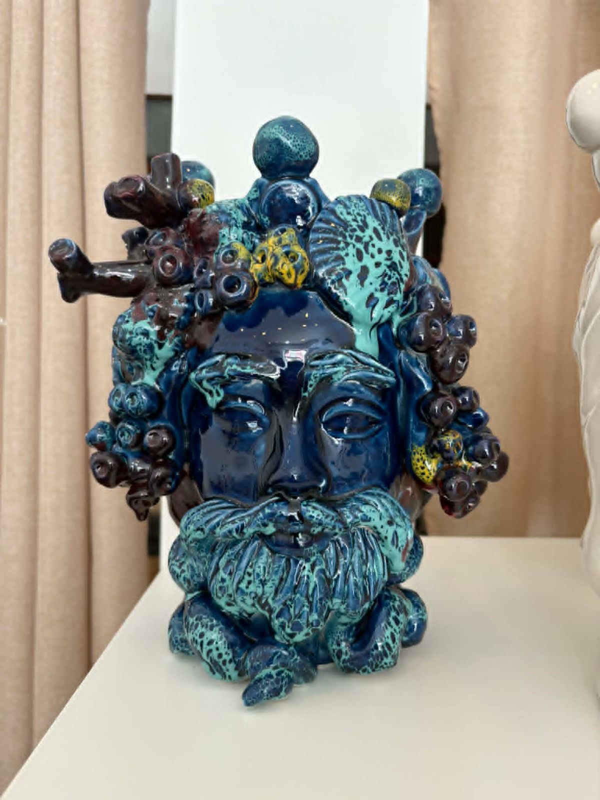 Sculture in ceramica blu e marrone esposte in una vetrina, tra cui un volto e forme simili ad alberi.
