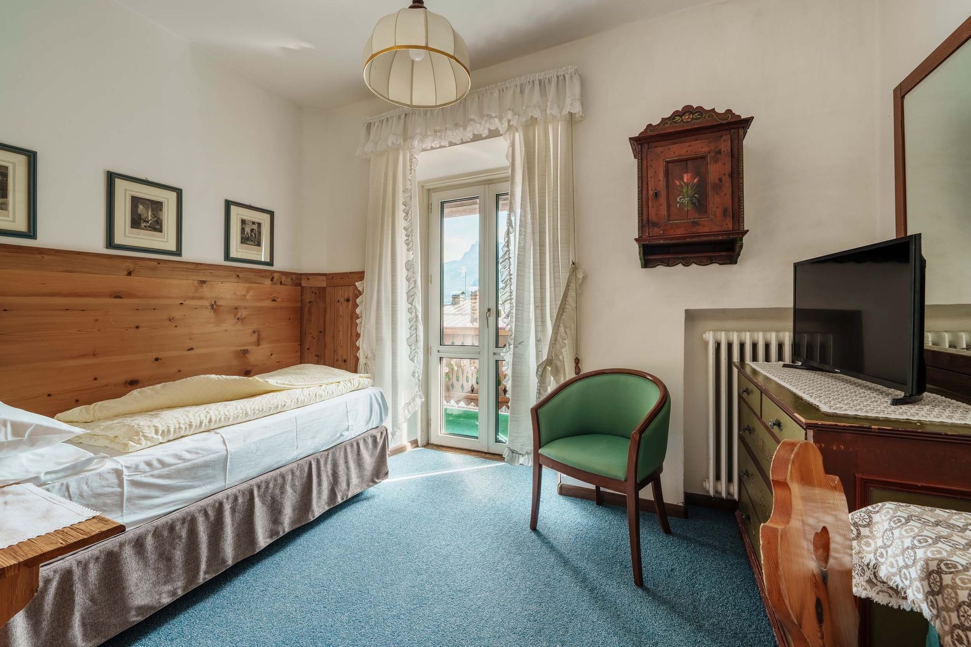 Una stanza d'albergo con un letto singolo, una sedia, una televisione e uno specchio.