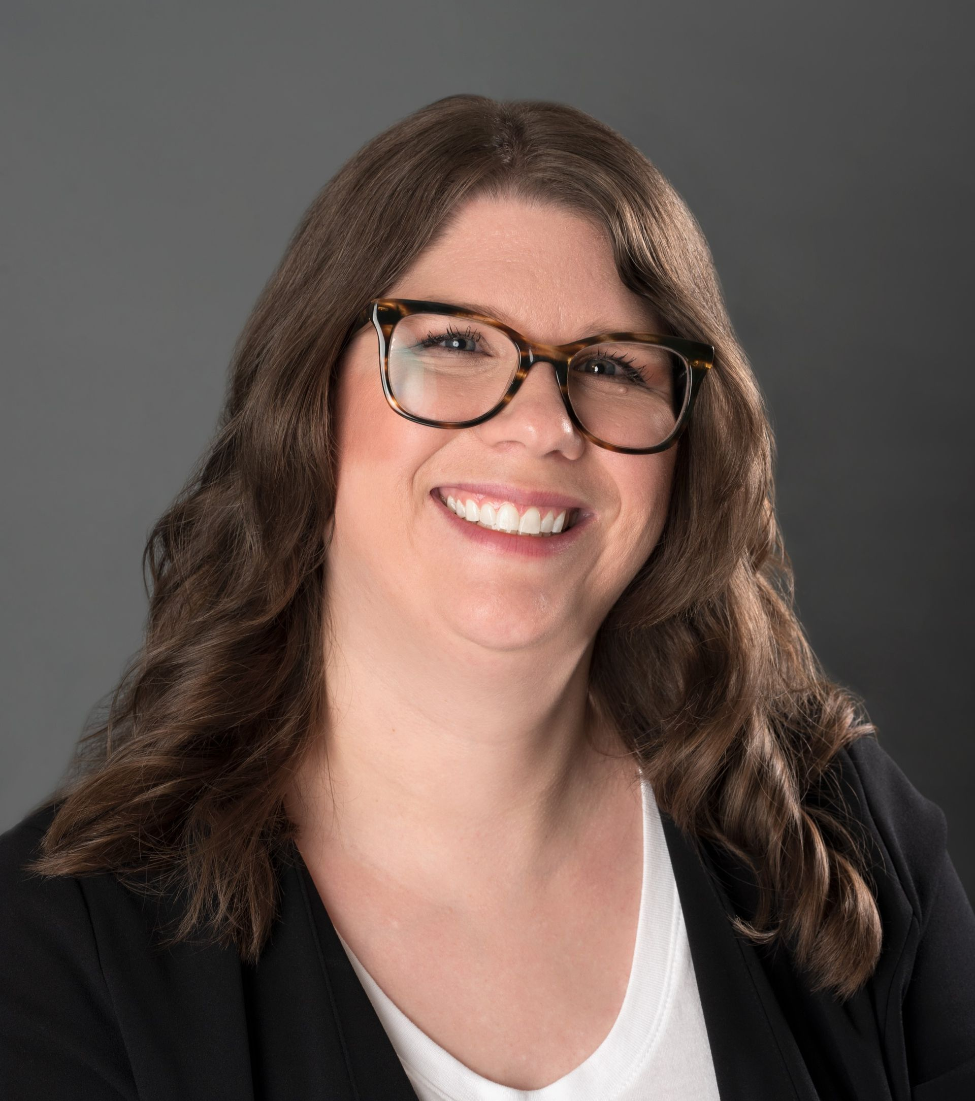 Woman with brown wavy hair and glasses smiles.