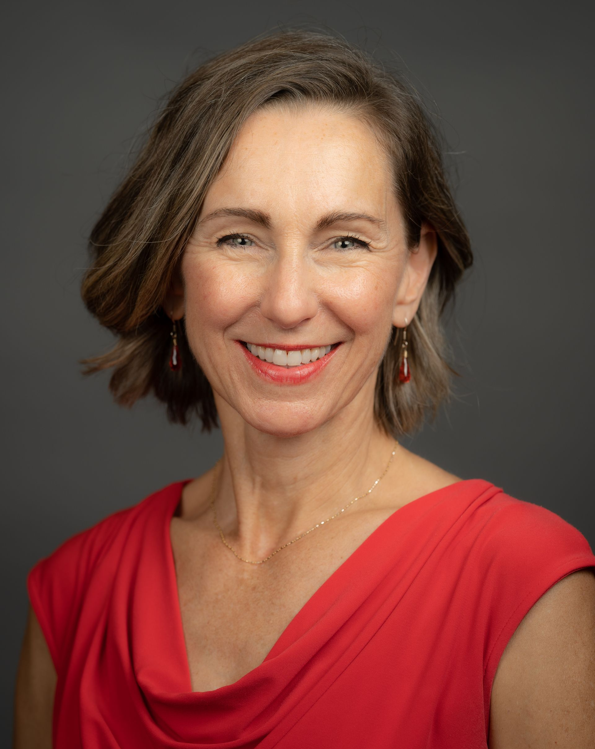 Woman with short, light brown hair wearing a red top smiles at the camera.