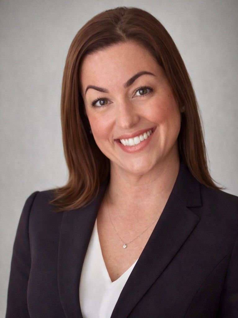 Woman with light brown hair smiles, wearing black shirt against a pink background.