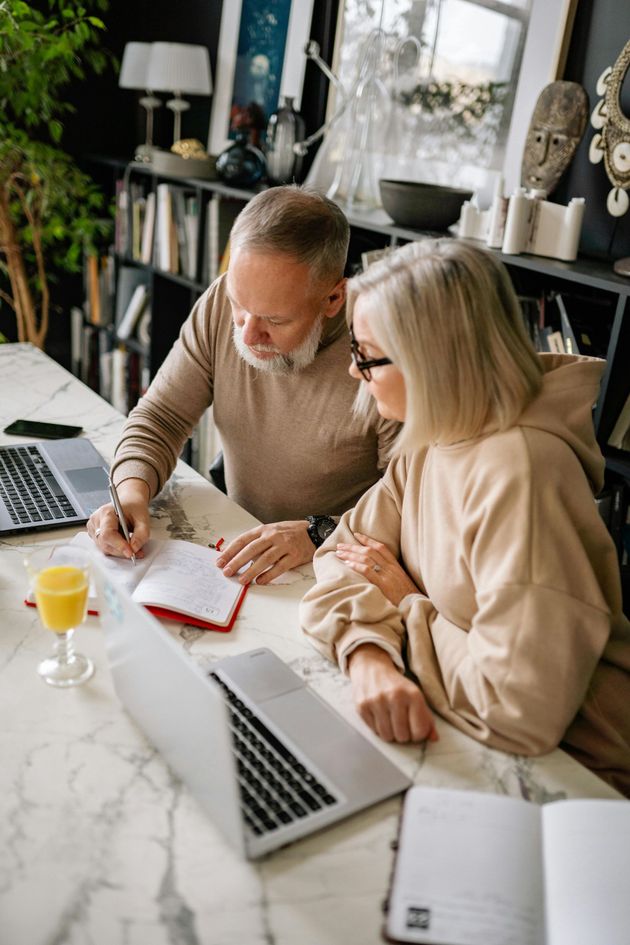 Couple working together at a table with laptops, paperwork, and drinks.